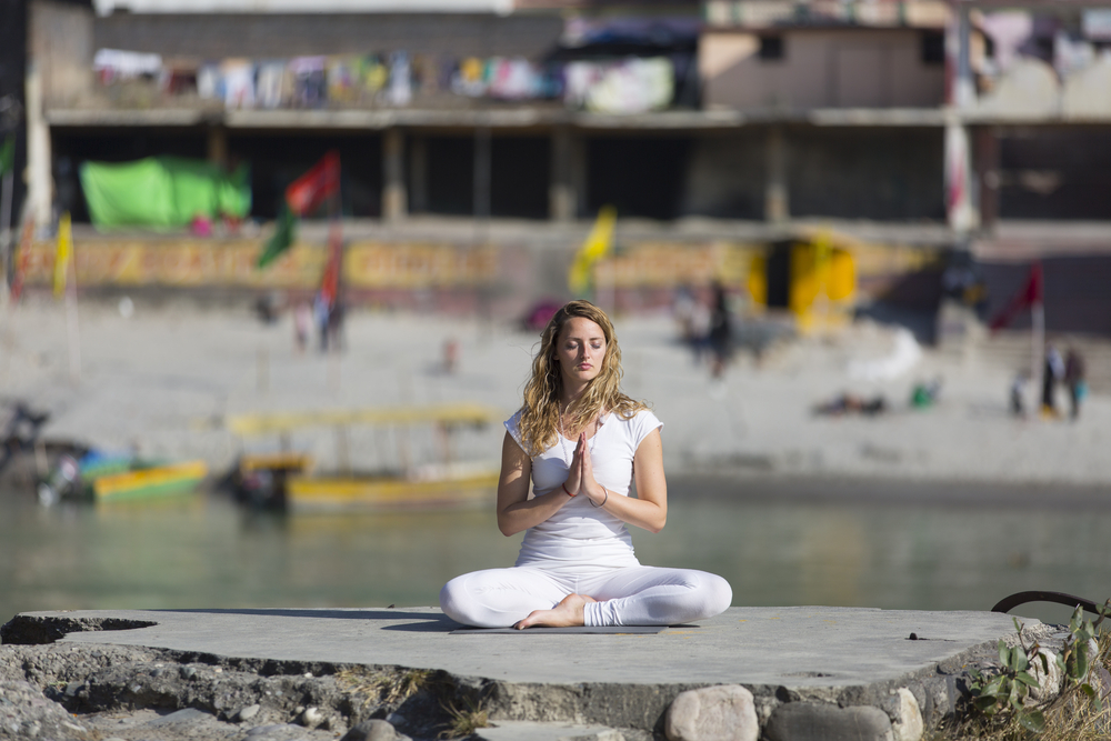 Woman in white dress sitting in half lotus pose in Rishikesh